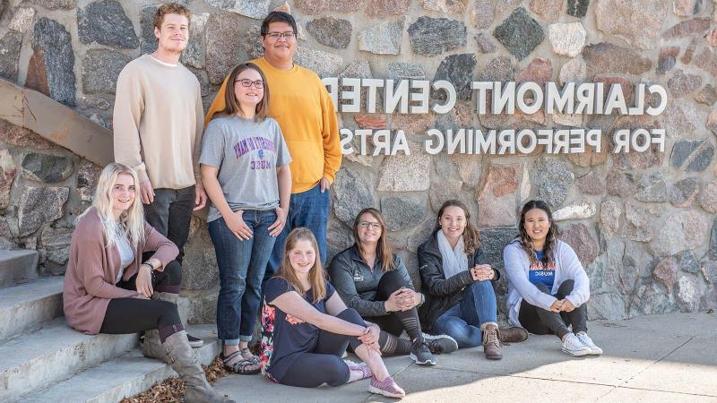 Group of smiling students by the Clairmont for Performing Arts signage on the exterior of the building